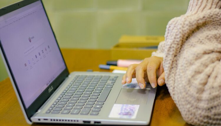 Close-up of a student using a laptop with stationery on a wooden desk in a cozy indoor setting.